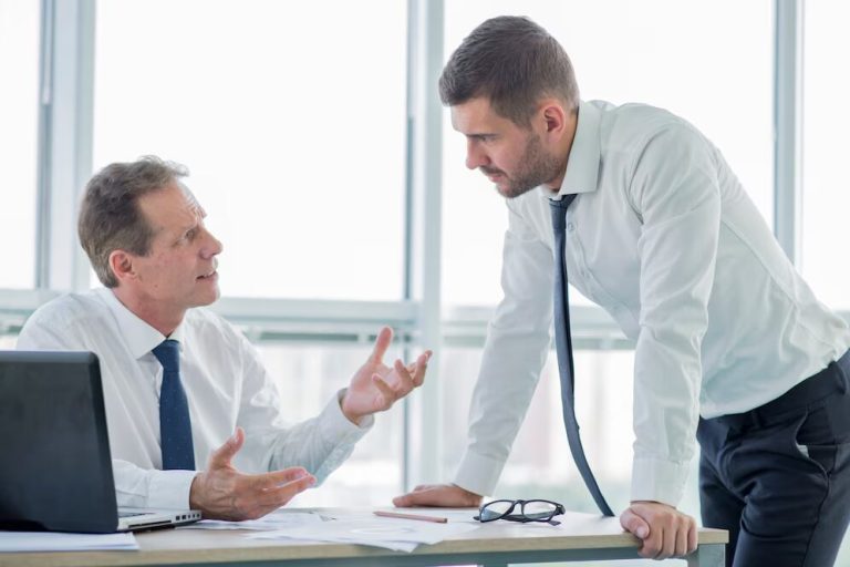 A person sitting at their desk talking to a person who’s standing