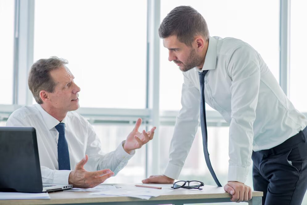 A person sitting at their desk talking to a person who’s standing
