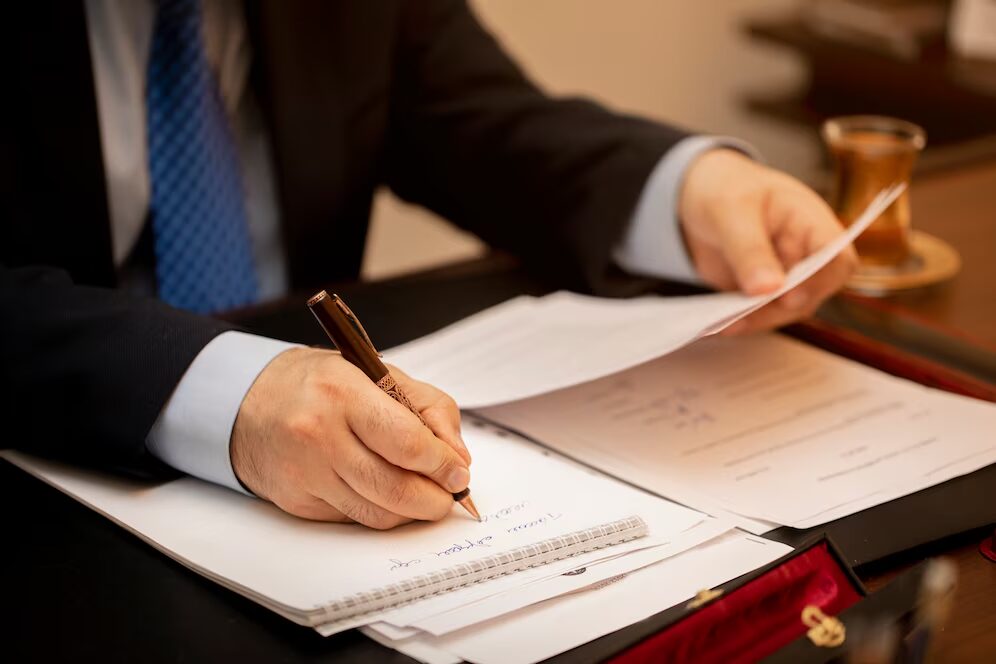 A person writing in their notebook while looking at papers