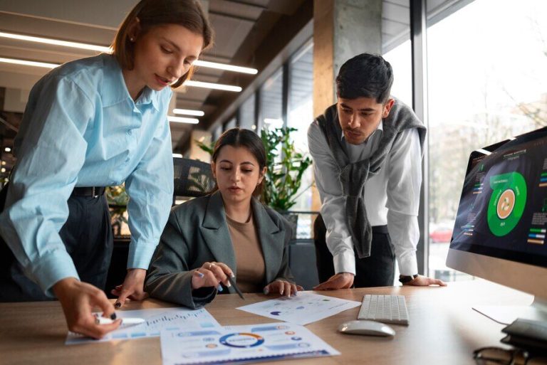 Three people reviewing graphs on papers, placed on a desk with a desktop
