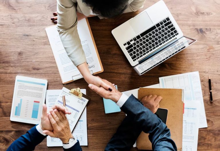 Two people shaking hands with papers and files in the background