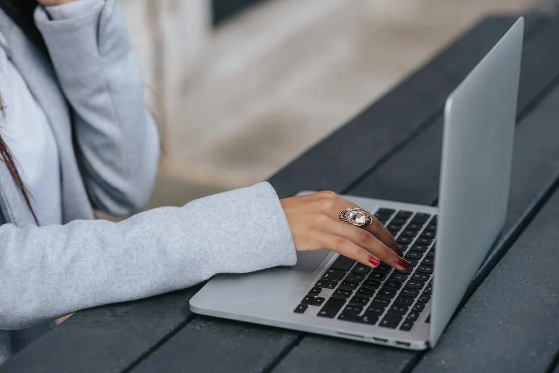 A cropped image of a businesswoman typing on a laptop at an outdoor street table.