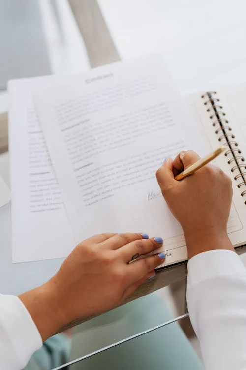 A person signing a contract with a black pen on a desk.