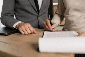 A person signing a contract with a pen on a clipboard.