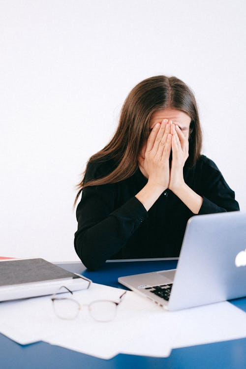 A stressed woman sitting with her hands covering her face.