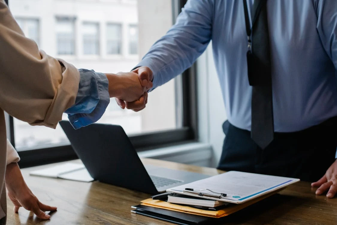 People shaking hands over a clipboard and laptop