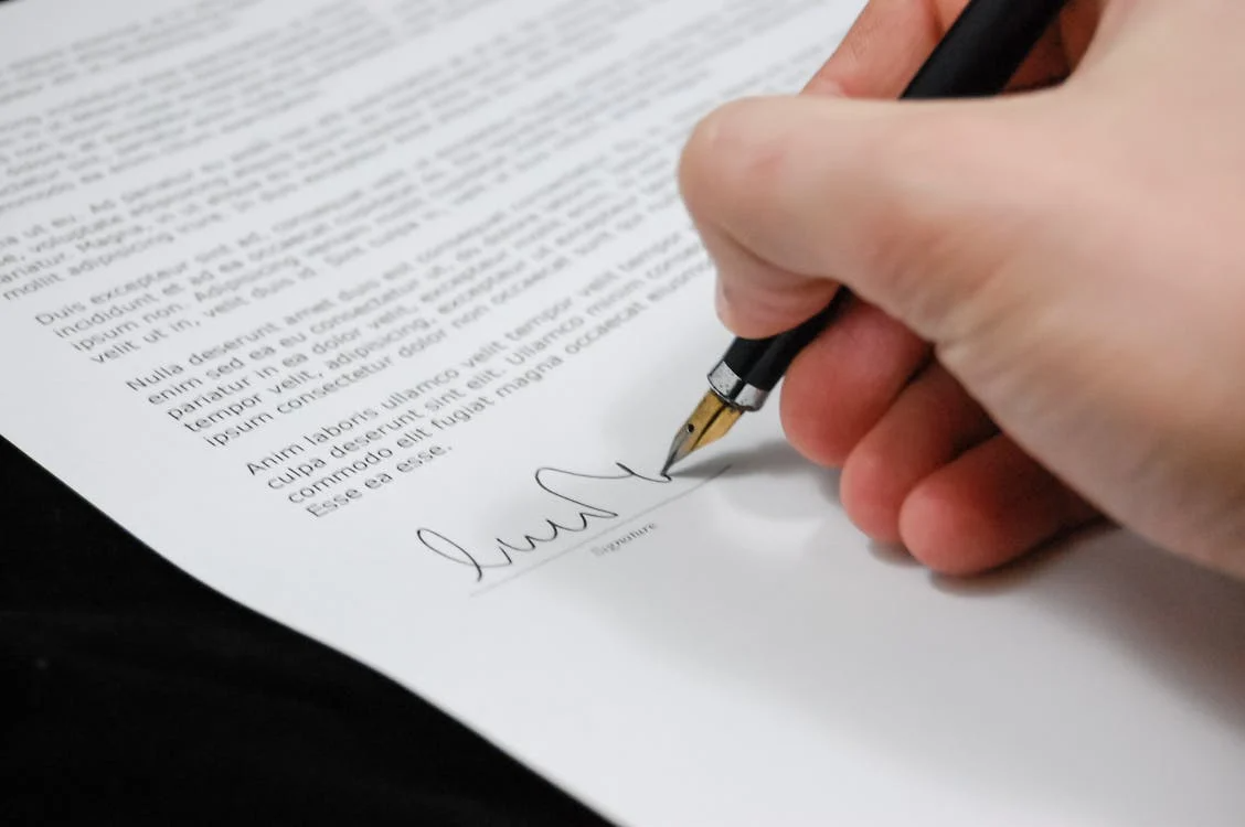 Person signing an official document on a desk.
