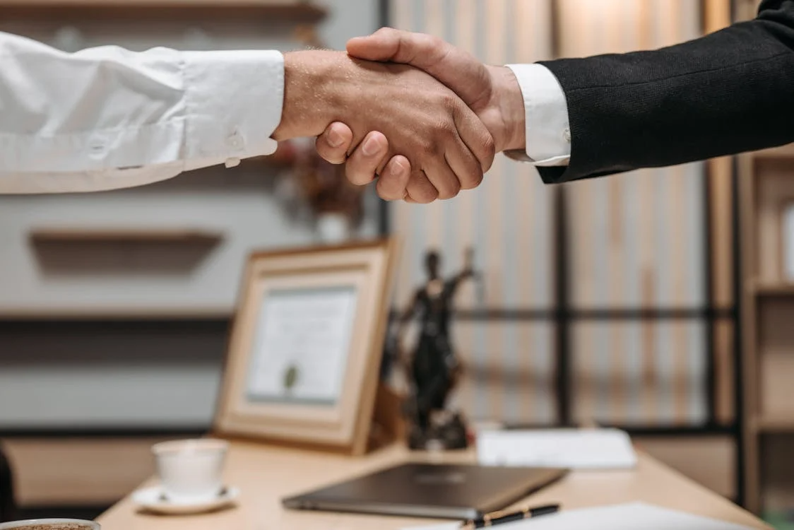 Two people in business attire shaking hands across a table.