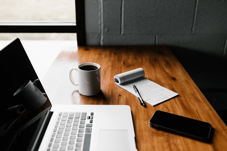 a laptop, coffee, and a notepad on a table