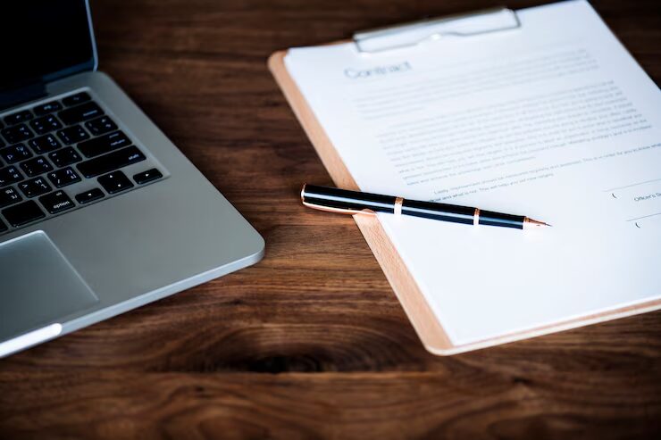 A contract, a pen, and a laptop placed on a desk
