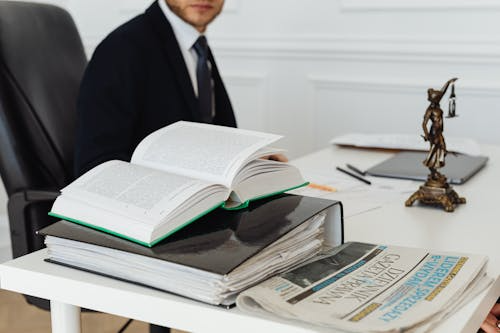 A Lady of Justice statue and books on a table with a lawyer sitting on a chair