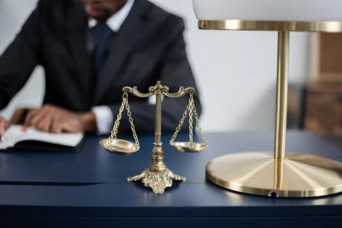 A justice scale on a table with a lawyer sitting at the back