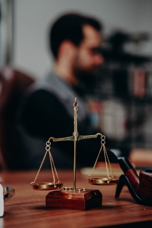 A justice scale on a table with an attorney sitting at the back, working