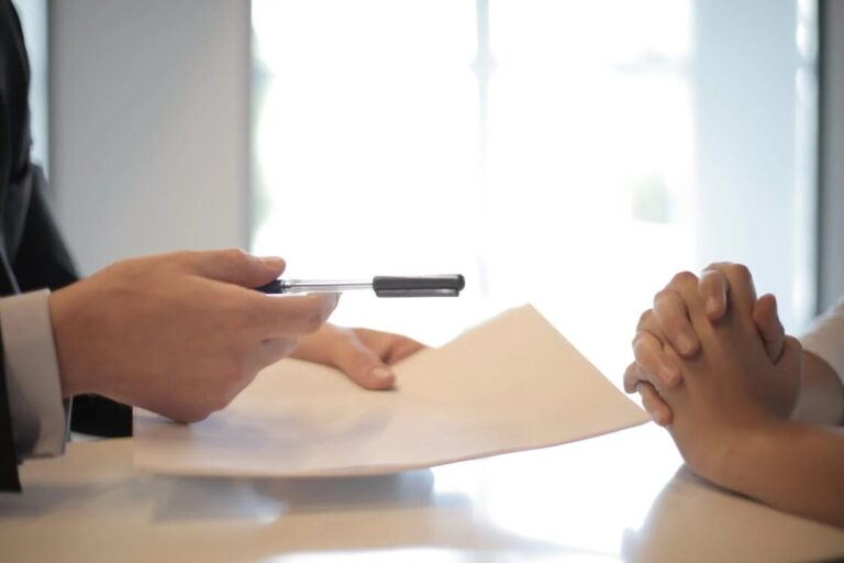 A man handing over a pen and a piece of paper to another person