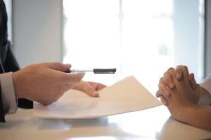 A person handing over a pen and paper to another over a table
