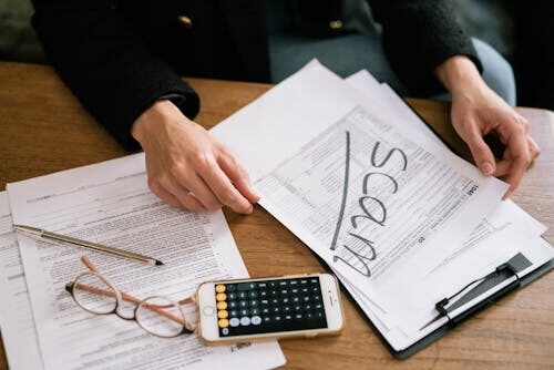 A person holding documents with “scam” written on it and a calculator, glasses, and a pen on the side