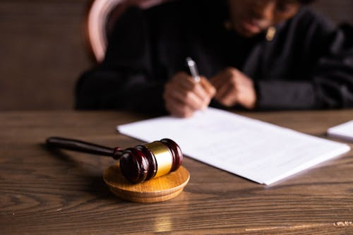 A wooden gavel on a surface with a lawyer signing documents in the background