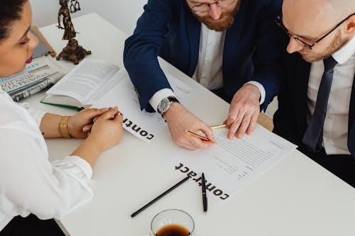 Three people examining a contract in a lawyer’s office with a Lady of Justice statue on the table