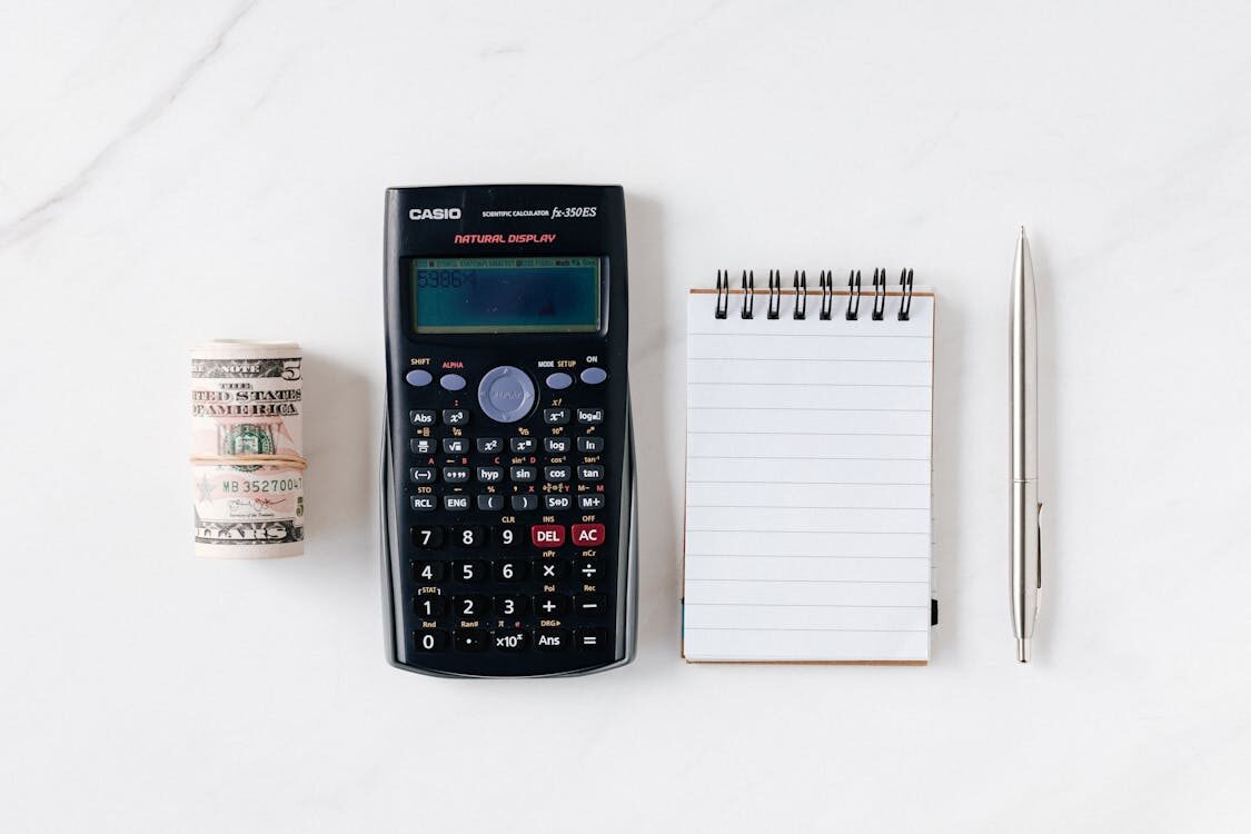 A calculator next to a notebook, pen, and money