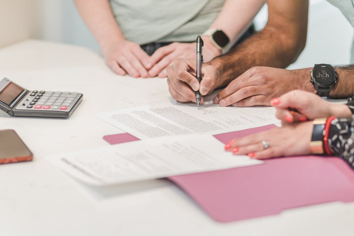 A person signing a contract next to two other people