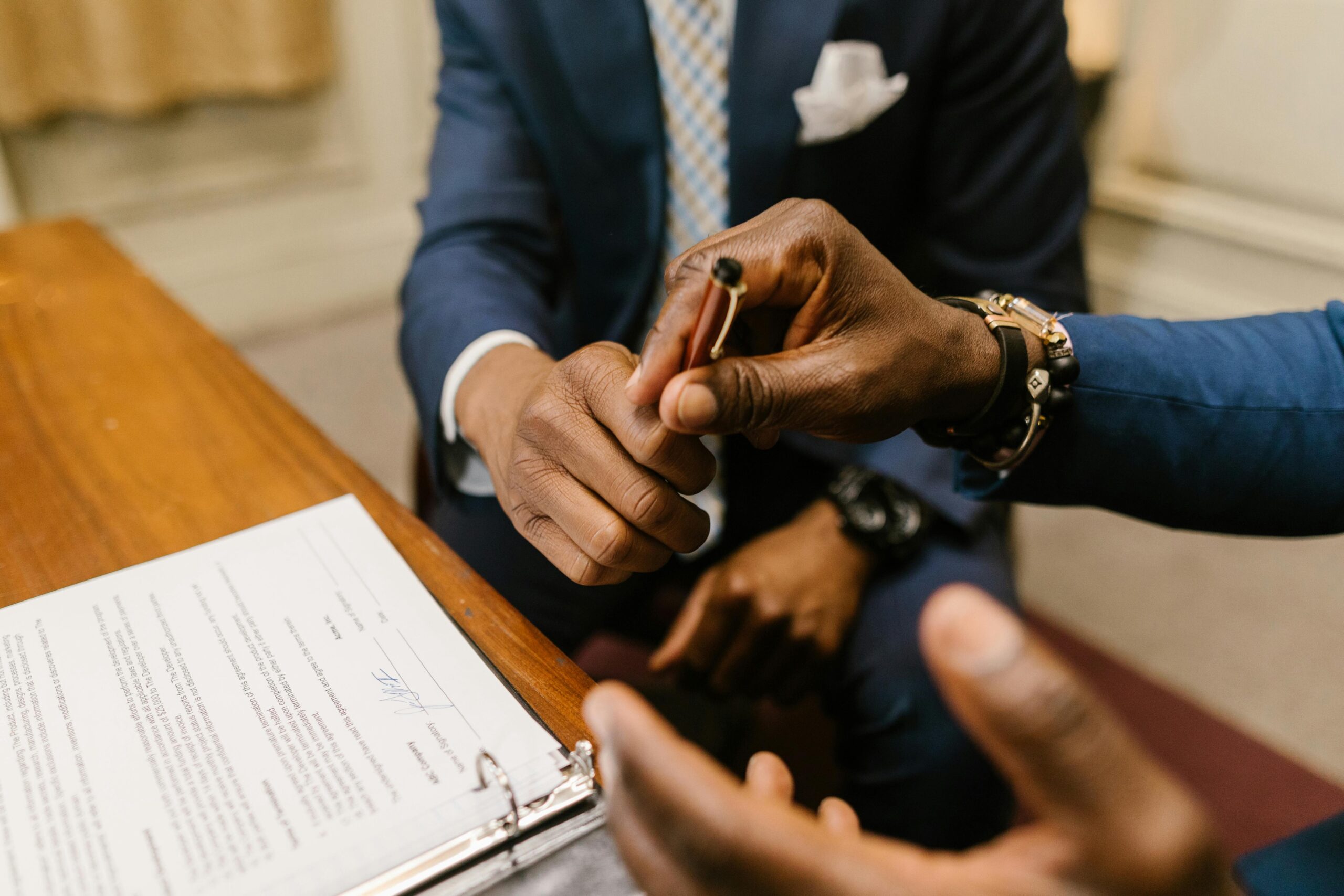 A person handing over a pen to another person to sign the papers