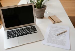 This image shows a laptop near the plant and documents with a pen on the table.