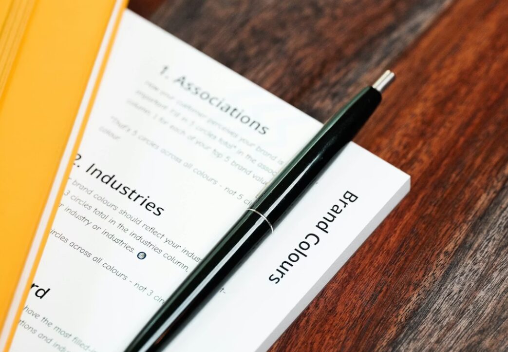This image shows business documents with a pen lying on a brown table.