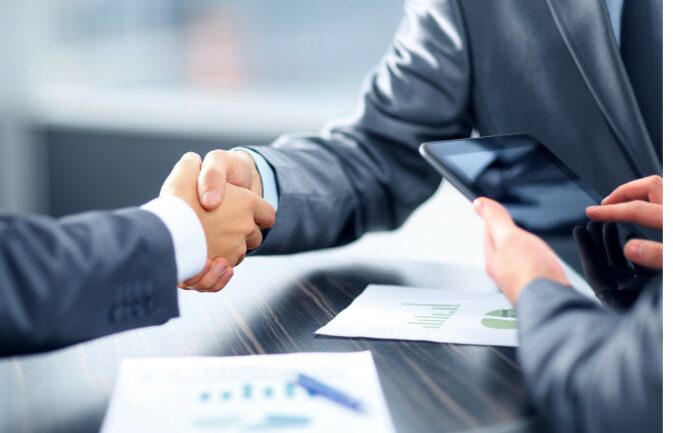This photo shows two professionals shaking hands over documents.