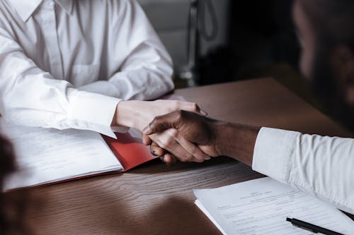 Two people shaking hands over a file with papers
