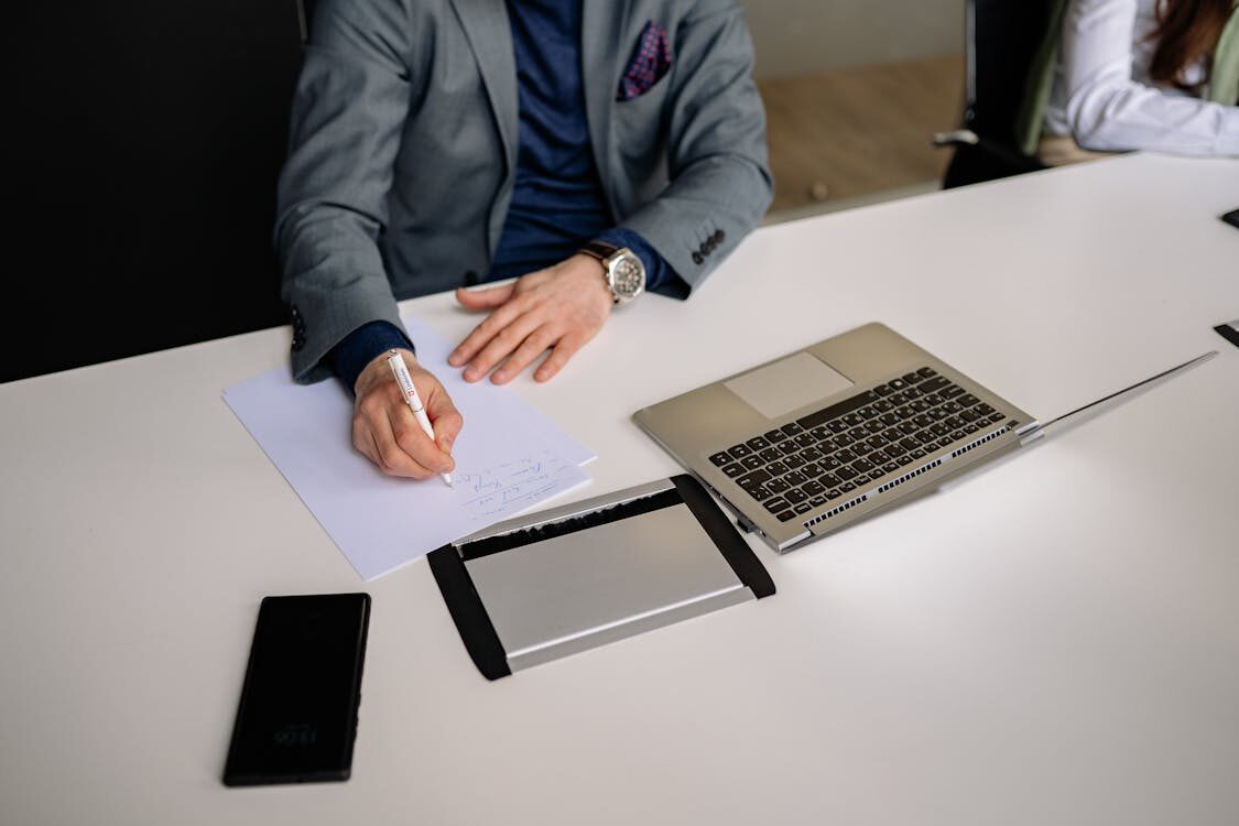 A person writing on papers with a laptop in the background