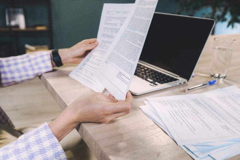 A person reviewing papers in front of their laptop