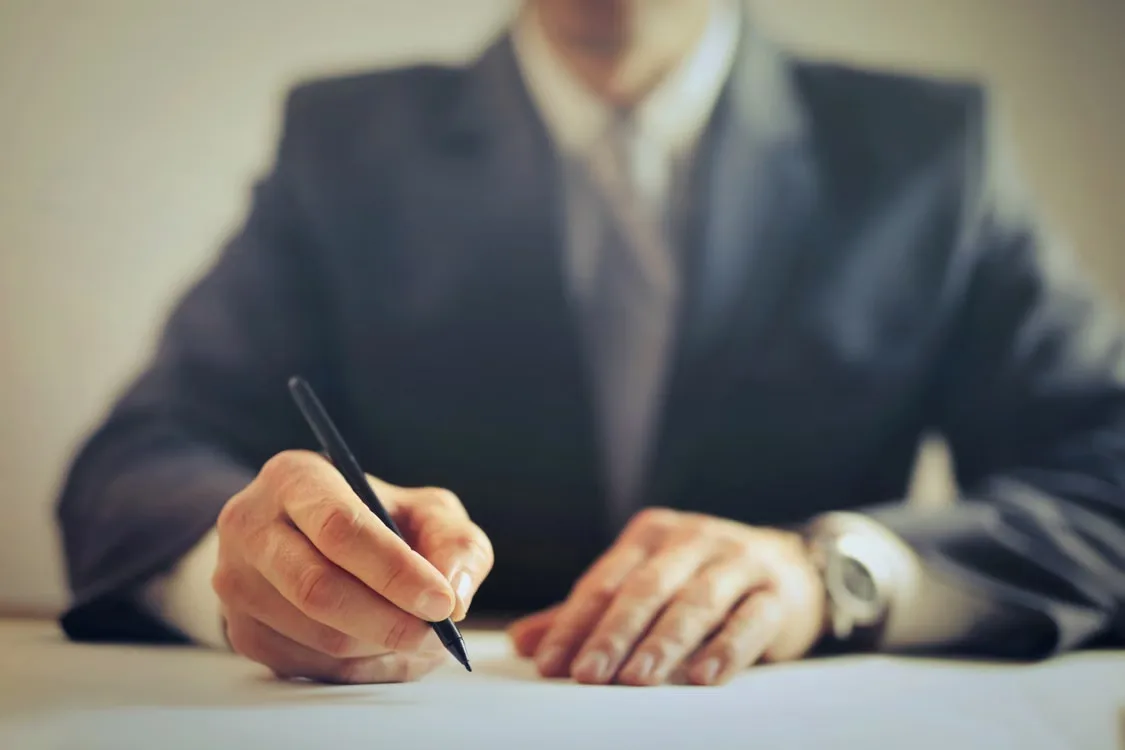 Person in a business suit signing a document with a pen at a desk