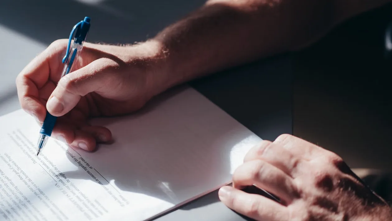 Person signing a commercial contract with a pen while another hand holds the document