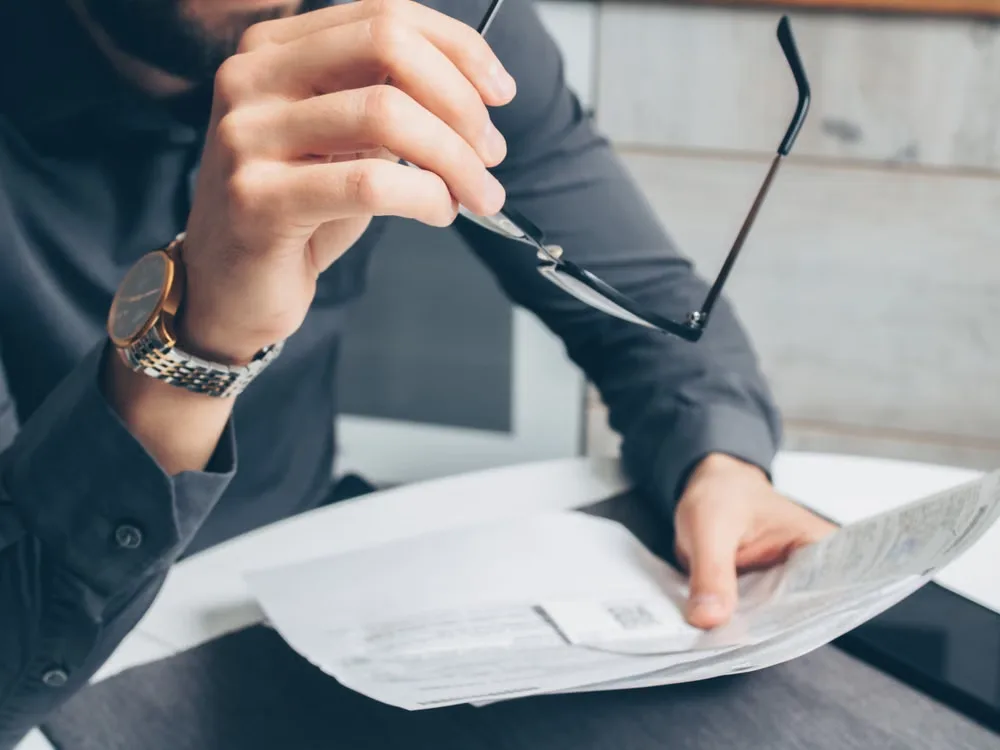 Business professional reviewing contract documents at a desk while holding eyeglasses
