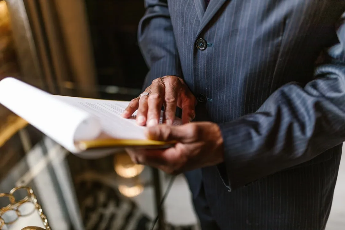Person in a dark suit examining paperwork inside a folder while reviewing business documents